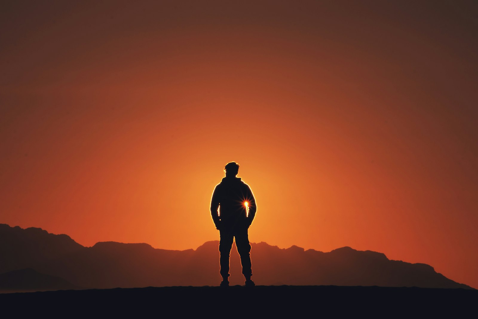 A person standing at golden hour with mountains behind them